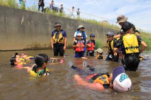 水辺の自然塾で救命胴衣での浮き方を学ぶ児童の写真