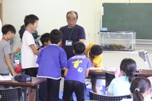 水辺の自然塾で採取した水生生物を見ながら座学を行う児童の写真