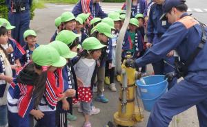 消火栓から出る水を見学する愛保育園幼年消防クラブの園児たちの写真