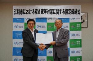 江別市長と江別不動産業協会会長が、「江別市における空き家等対策に関する協定書」を掲げ、握手しています。